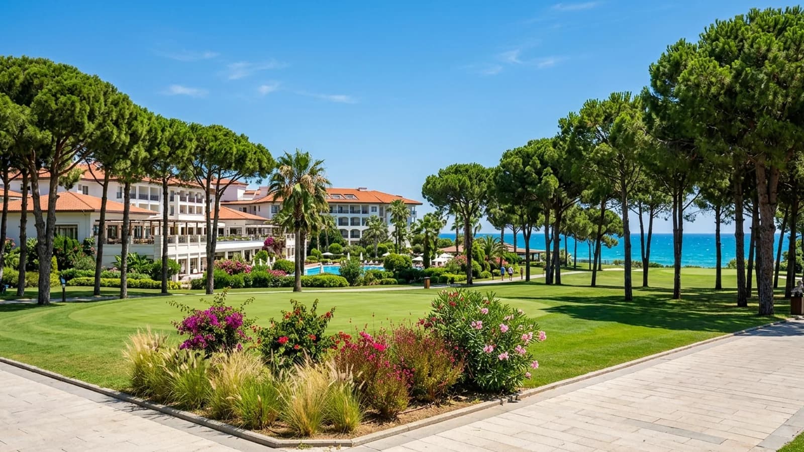 A sunny golf course fairway in Belek lined with pine trees, with a resort and sea beyond.